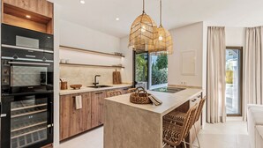 A modern kitchen with a central island, built-in oven, and a hanging rattan light fixture. - Beachside living in a charming urbanisation (Marbella)
