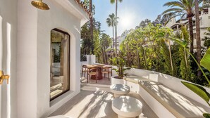 A modern outdoor patio with a dining area, seating, and a view of surrounding greenery. - Beachside living in a charming urbanisation (Marbella)