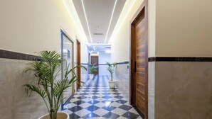 A hotel hallway with a checkered floor, potted plants, wooden doors, and a ceiling light. - Hotel Urban Lion - Delhi Airport (New Delhi)