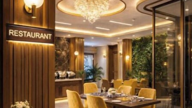 A restaurant interior with a wooden reception desk, a chandelier, yellow chairs, and a dining table set for four. - Hotel Urban Lion - Delhi Airport (New Delhi)