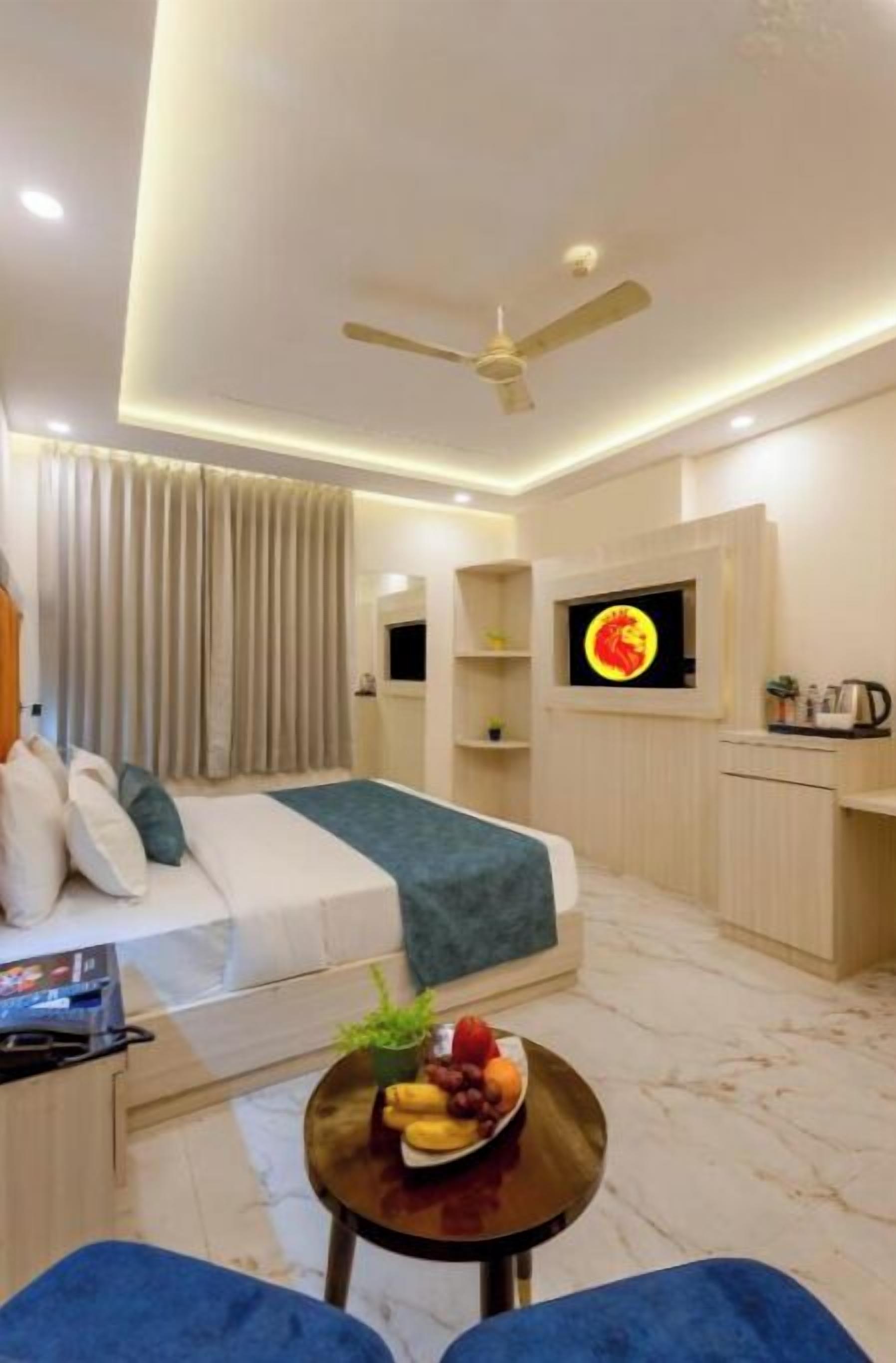 A modern hotel room with a bed, a desk, a TV, and a small table with fruit.