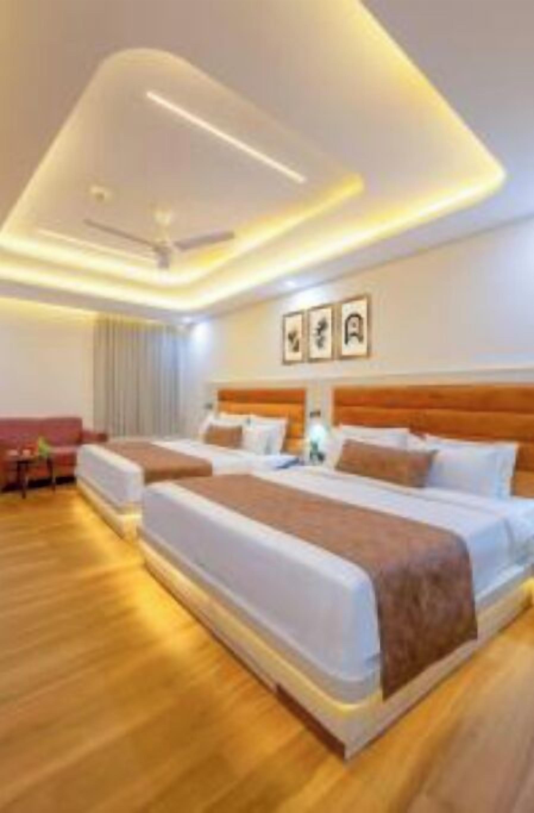 A hotel room with two beds, a wooden floor, a sofa, and a ceiling with recessed lighting.