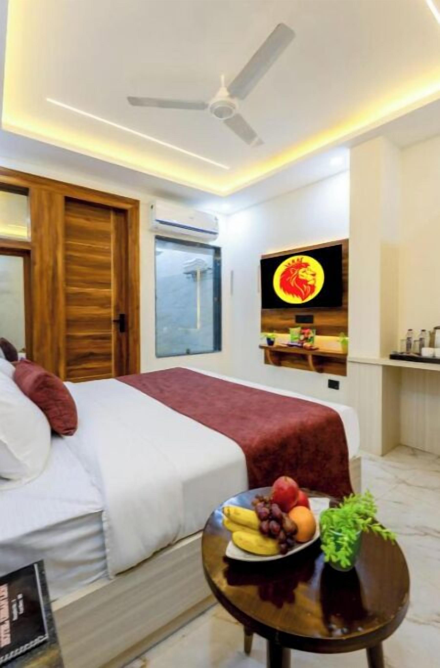 A hotel room with a bed, a TV mounted on the wall, a wooden door, and a small table with fruit.