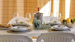 Una mesa de comedor dispuesta con platos, vasos, una botella de vino y un frutero.