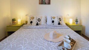 Una cama bien hecha con una colcha estampada, dos lámparas de noche, una obra de arte en la pared y una planta en la mesita.
