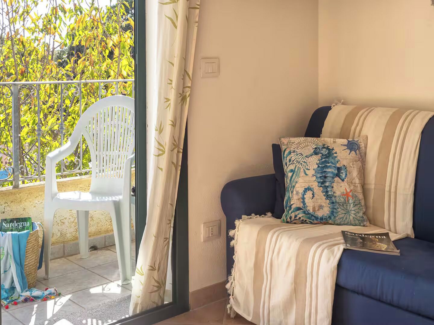 A room with a blue sofa, a white chair, a patterned pillow, and a book on the sofa.