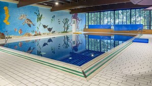 Una piscina interior con un mural de vida marina en la pared, vistas despejadas del exterior a través de amplias ventanas y una zona de estar con cojines azules.