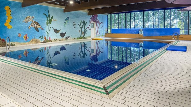 Una piscina interior con un mural de vida marina en las paredes, vistas despejadas del exterior a través de amplias ventanas y suelo de baldosas.