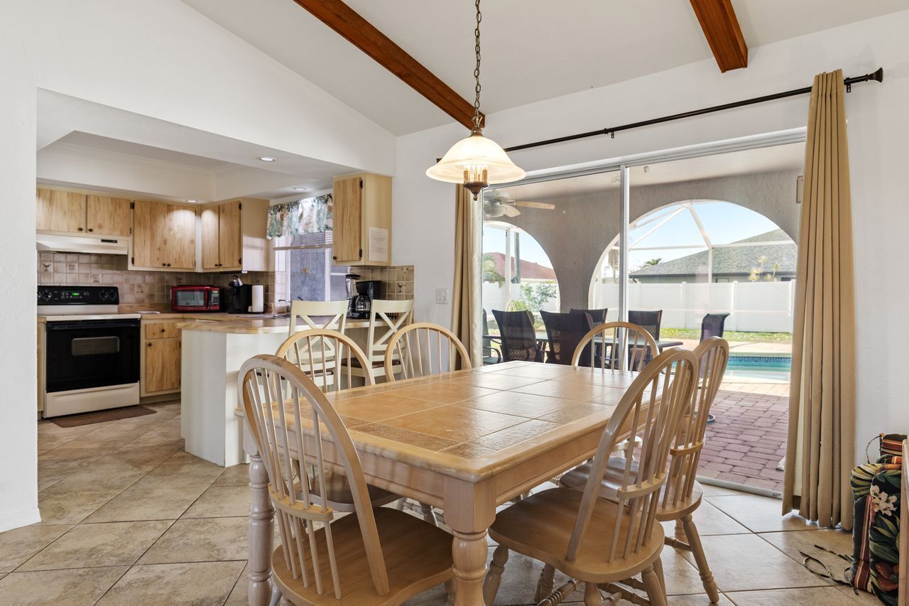 A kitchen with wooden cabinets, a dining table with chairs, a hanging light fixture, and a view of a swimming pool through glass doors.