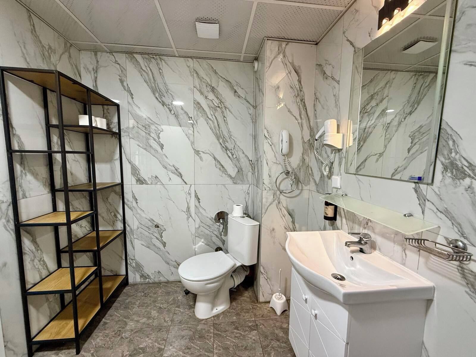 Een badkamer met marmeren wanden, een toilet, een wastafel, een spiegel en een plankunit.