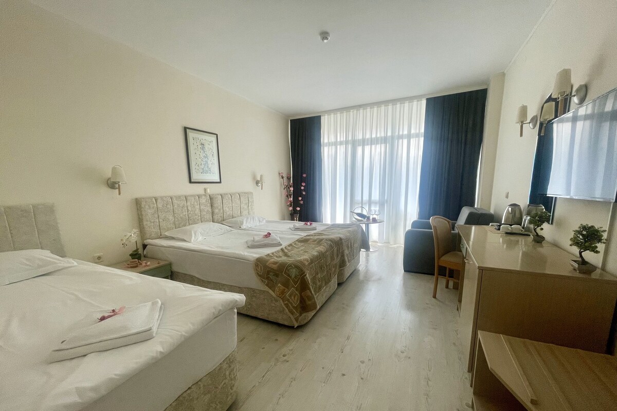 Une chambre d’hôtel avec deux lits, un bureau, une chaise, une petite table et une fenêtre avec des rideaux.