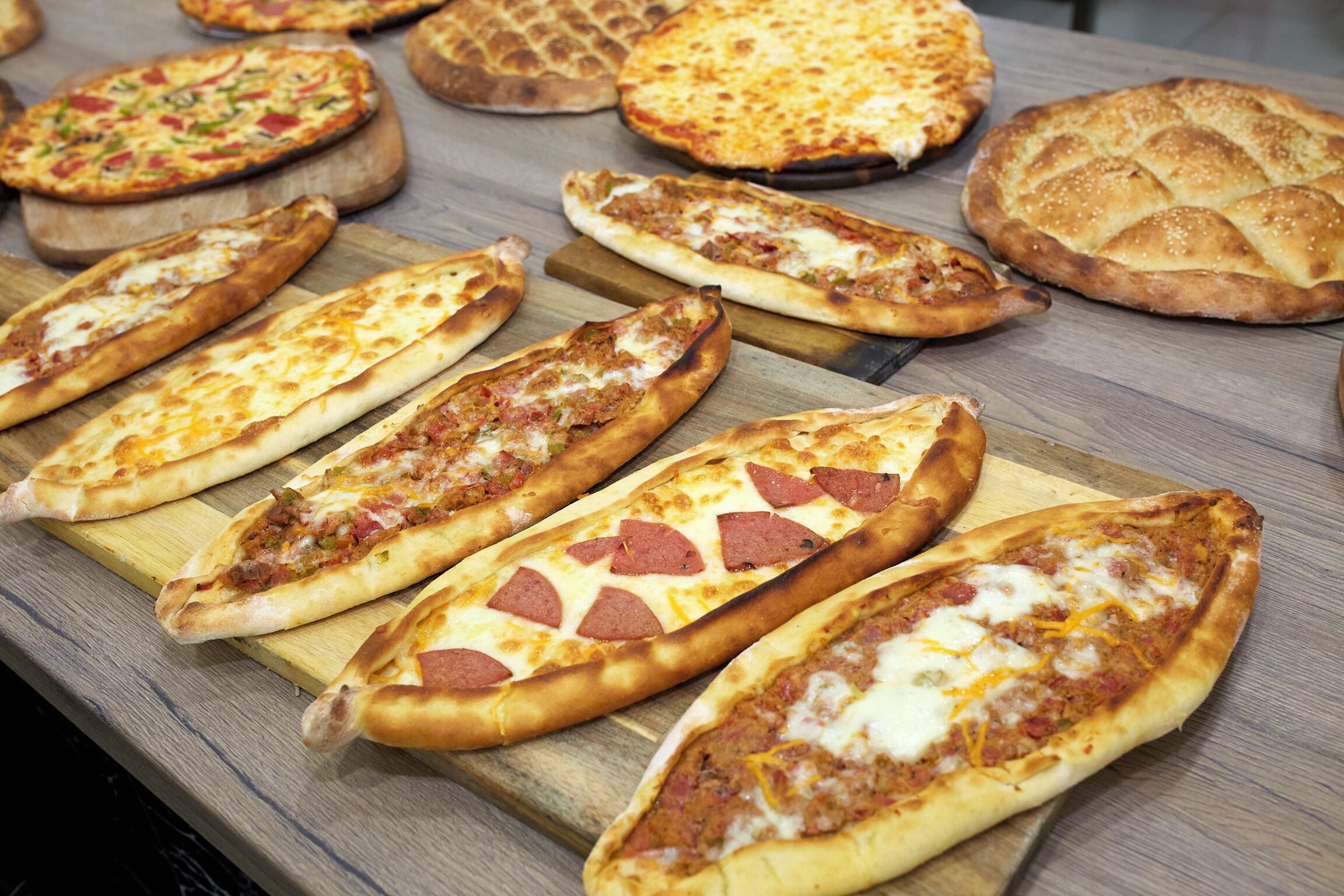 A variety of flatbreads and pizzas on wooden boards.