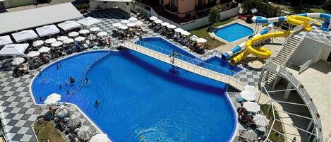 A large outdoor swimming pool with a checkered deck, a water slide, and lounge areas with umbrellas.