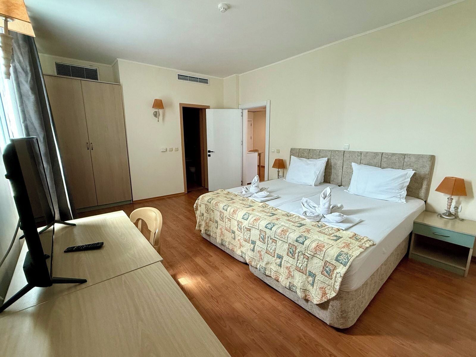 A hotel room with a bed, a desk, a chair, a TV, and a wardrobe.