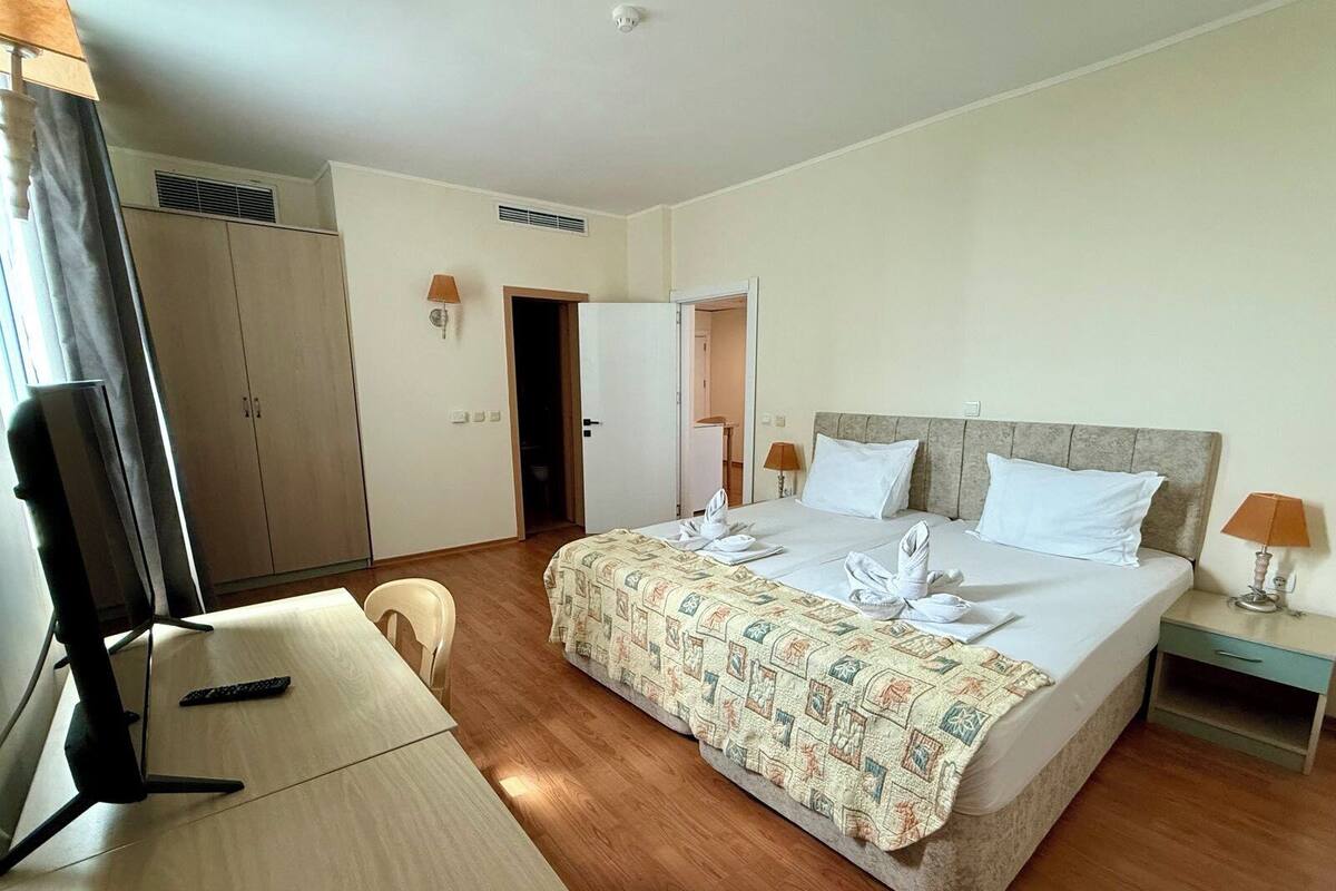 Una habitación de hotel con cama, escritorio, silla, televisor y armario.