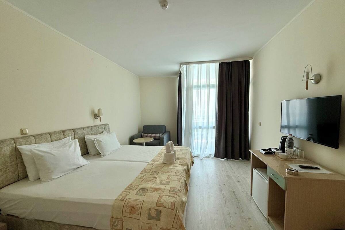Habitación de hotel con una cama grande, un escritorio con televisor, una silla y una ventana con cortinas.