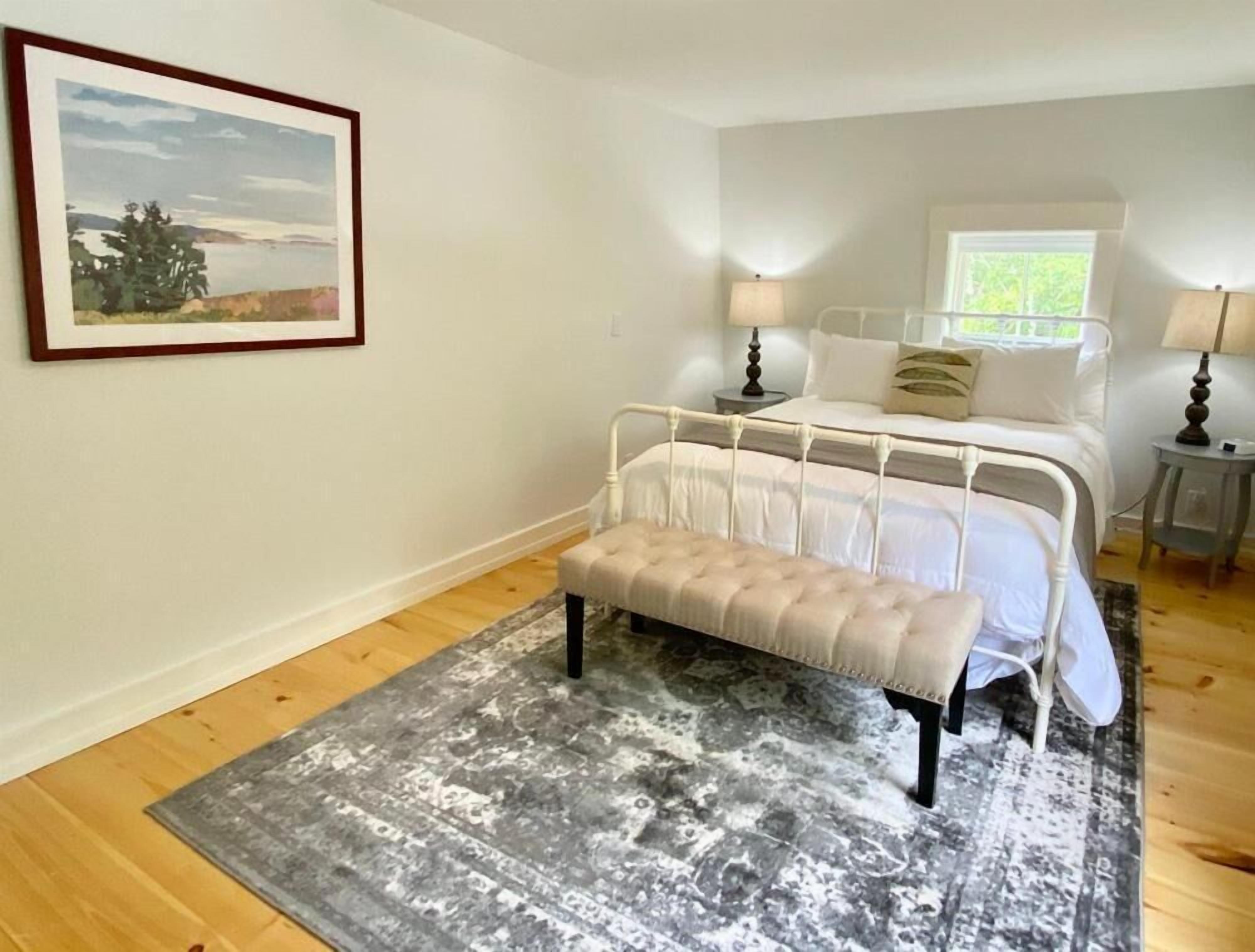 A bedroom with a bed, bedside tables, a bench, a rug, and a framed picture on the wall.