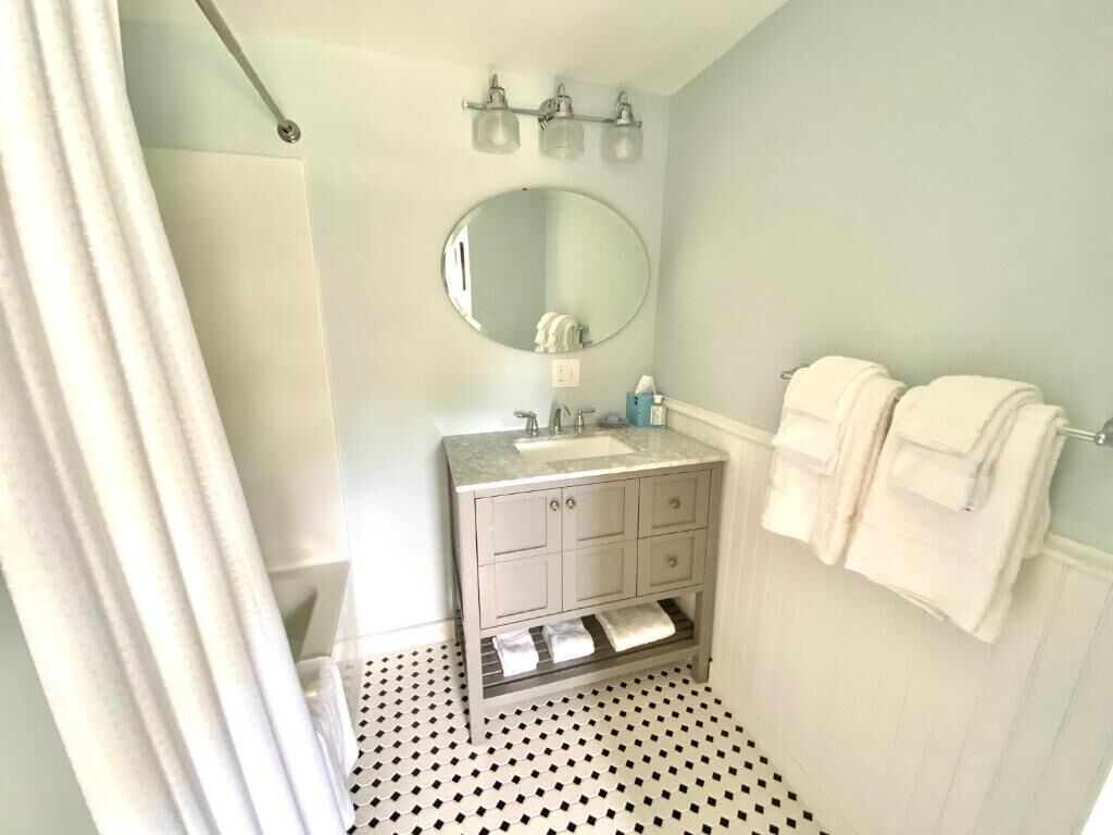 A bathroom with a shower, a sink, a mirror, and a towel rack.