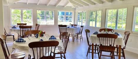 A spacious dining area with high ceilings and large windows, wooden chairs, and tables set for dining.