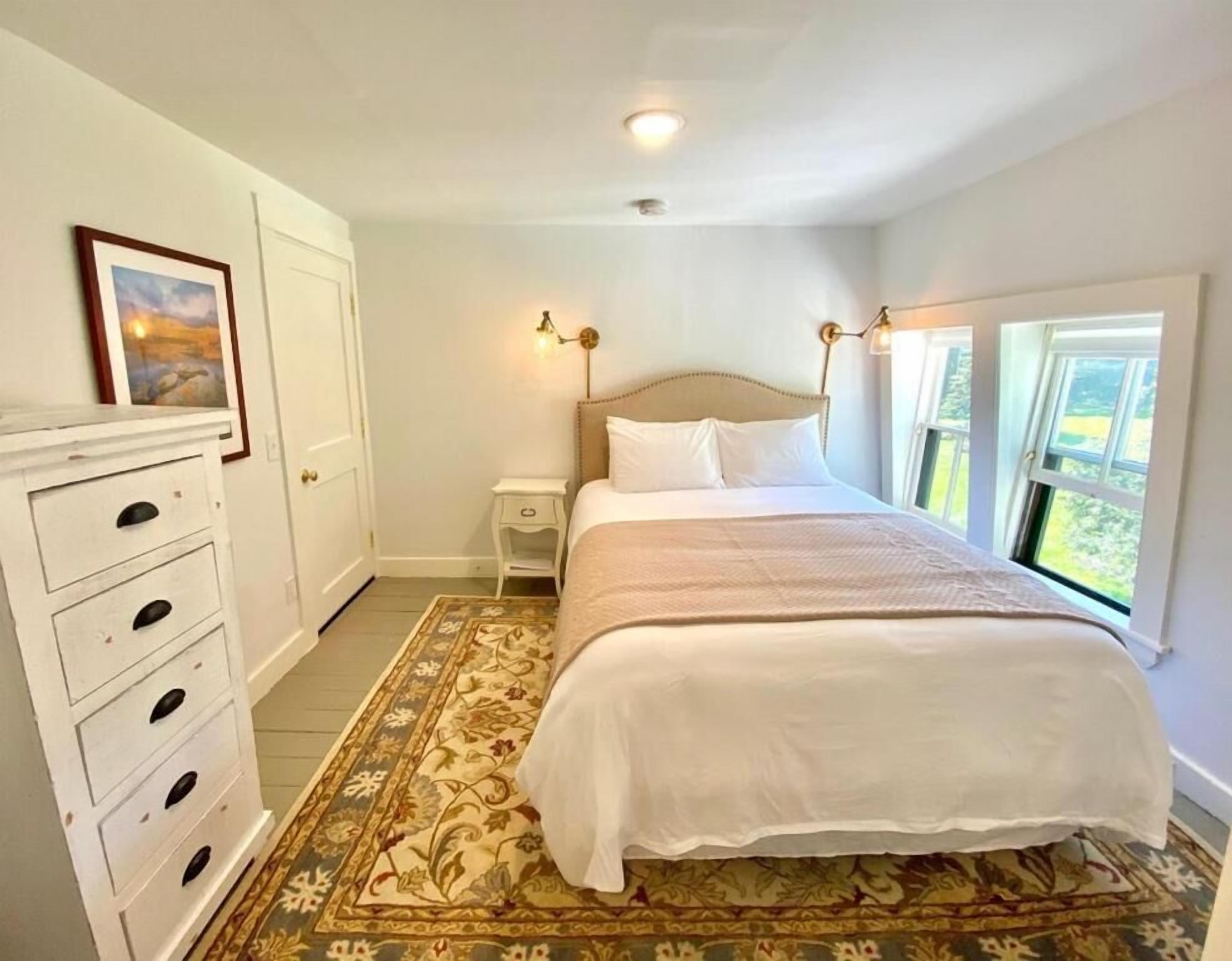 A bedroom with a bed, a nightstand, a dresser, a window with a view, and a ceiling light.