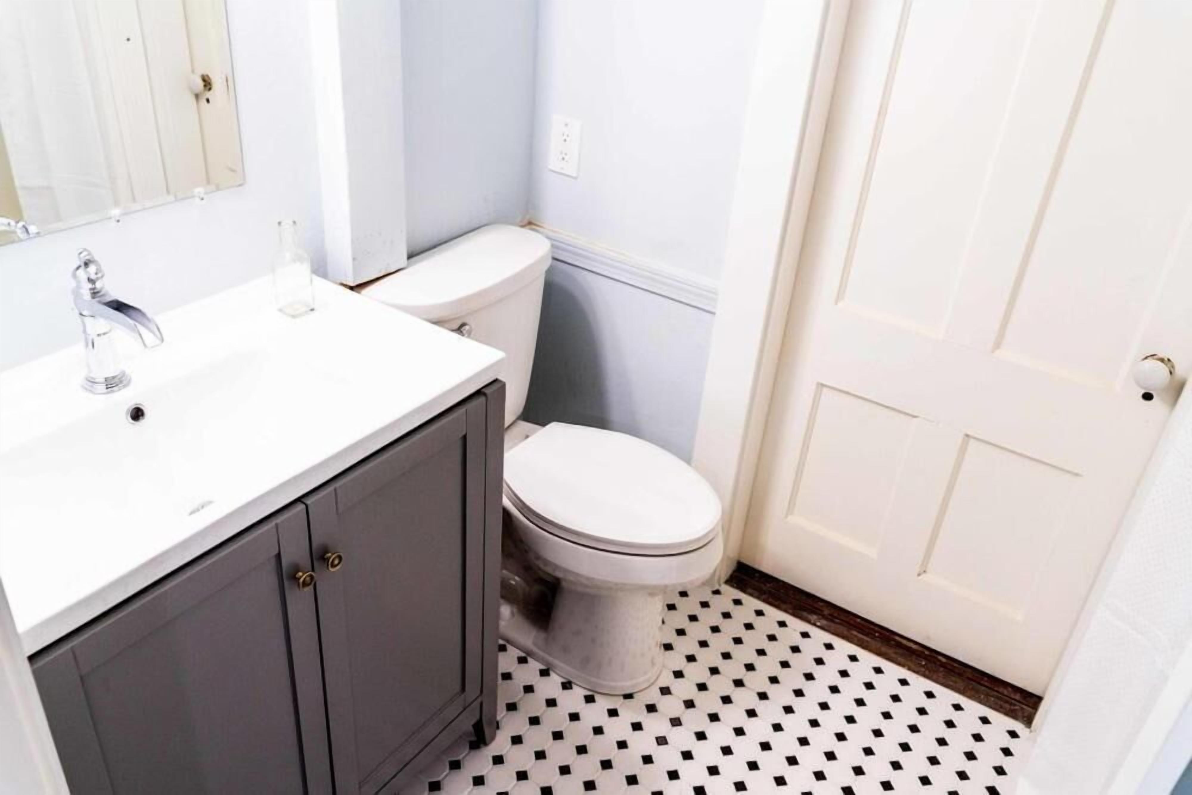 A bathroom with a white toilet, dark cabinets, a white sink, and a tiled floor.