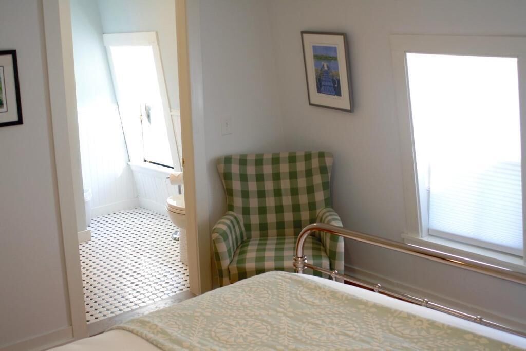 A room with a bed, a checkered chair, a window, and a door leading to another room.