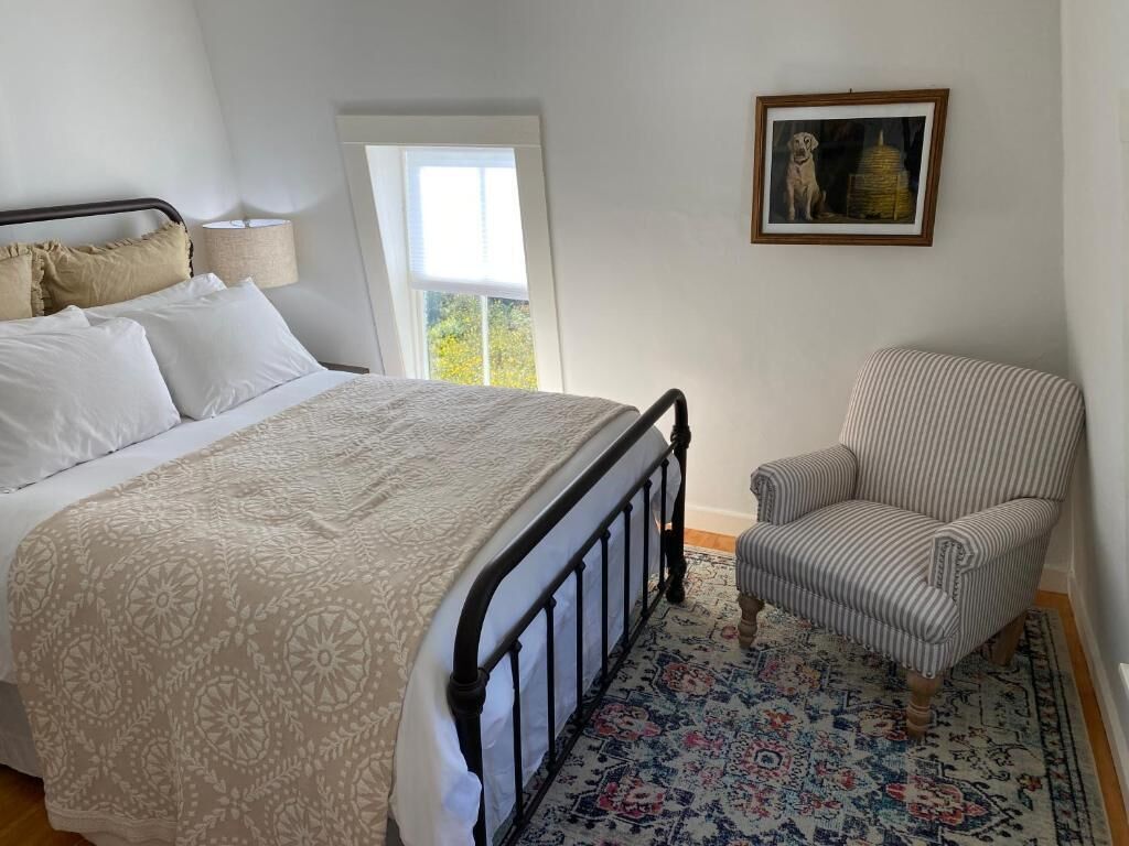 A bedroom with a bed, a chair, a window, and a framed picture on the wall.
