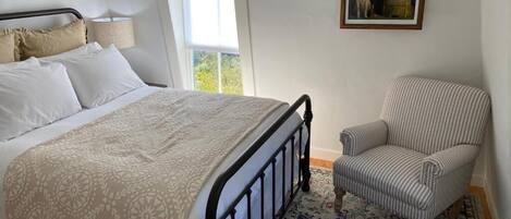 A bedroom with a bed, a chair, a window, and a framed picture on the wall.