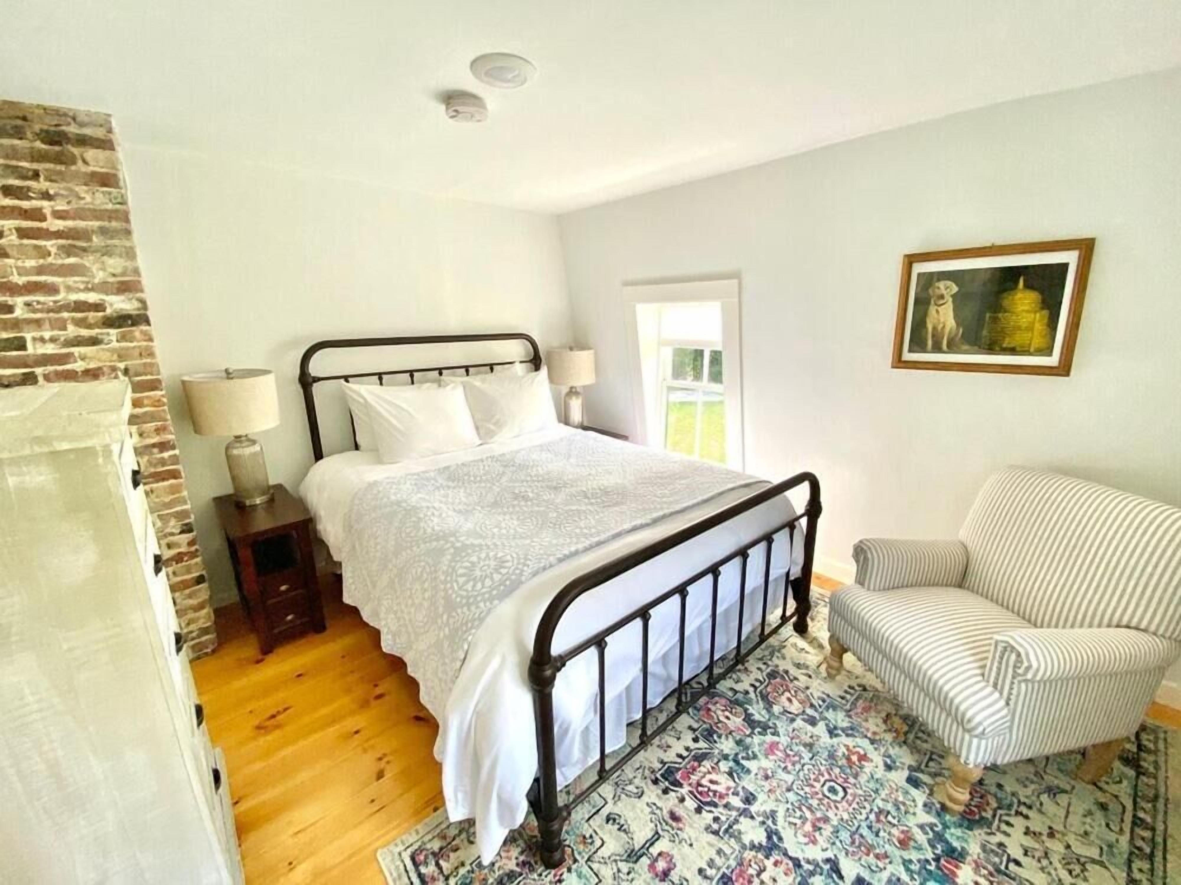 A bedroom with a bed, a chair, a lamp, a rug, and a painting on the wall.