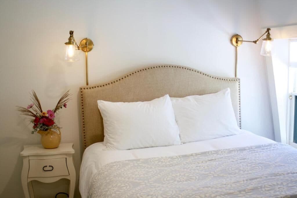 A neatly made bed with a patterned bedspread, a bedside table with a vase of flowers, and wall-mounted lighting fixtures.