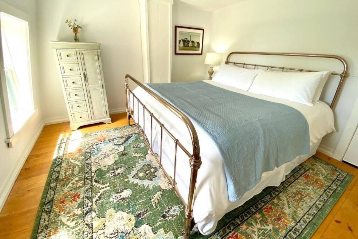 Ein Schlafzimmer mit einem Bett, einem Schminktisch, einer Lampe und einem gerahmten Bild an der Wand.