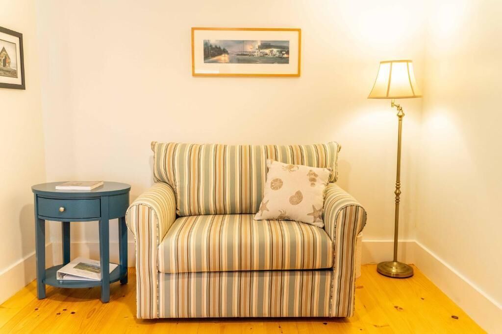A striped sofa with a cushion, a small round side table, a floor lamp, and a framed picture on the wall.