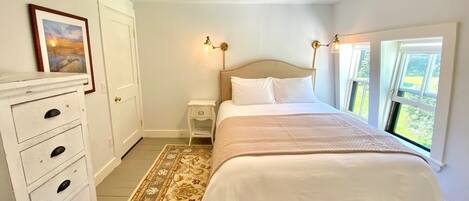 Un dormitorio con cama, mesitas de noche, cómoda, ventana con vistas y una lámpara en el techo.