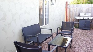 Eine Terrasse im Freien mit einem schwarzen Metalltisch und -stühlen, einem Grill und einem Holzzaun.