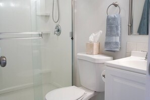 Een badkamer met een douchecabine van glas, een toilet met een doos tissues, en een wastafel met een handdoek aan een rek.
