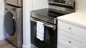 Eine kompakte Küche mit Edelstahlbackofen, einer Mikrowelle und einem übereinander angeordneten Waschtrockner.