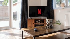 A living room with a TV displaying the Netflix logo, a wooden coffee table, and a small elephant figurine. - Modern Comfort |4BR House for 11| Central & Quite (Essex)
