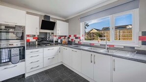 A modern kitchen with white cabinets, a built-in oven, a large window with a view of houses, and a tiled backsplash. - Modern Comfort |4BR House for 11| Central & Quite (Essex)