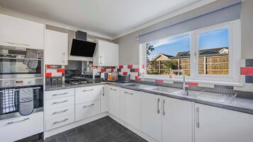A modern kitchen with white cabinets, a built-in oven, a large window with a view of houses, and a tiled backsplash.