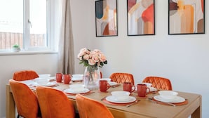 A dining area with a table set for six, orange chairs, a vase with flowers, and abstract art on the wall. - Modern Comfort |4BR House for 11| Central & Quite (Essex)
