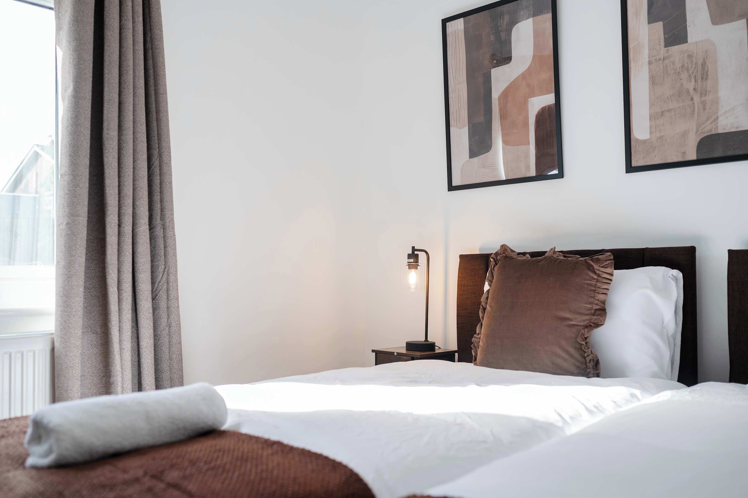 A hotel room with a bed, a nightstand with a lamp, and abstract wall art.