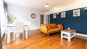 A living room with a sofa, dining table, chairs, a coffee table, and artwork on the wall.