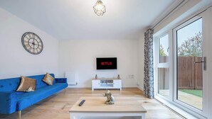 Ein Wohnzimmer mit einem blauen Sofa, einem weißen Couchtisch, einer dekorativen Elefantenfigur, einer Wanduhr und einem Fernseher, der 'NETFLIX' anzeigt.