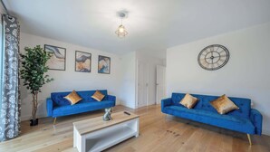 Ein Wohnzimmer mit zwei blauen Sofas, einem Couchtisch, einer Topfpflanze und einer Wanduhr.