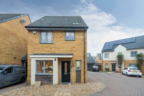 A two-story residential building with a brick facade, a black door, and a small window. - 3 BR House | Driveway Parking | Modern Comfort (Hertfordshire)