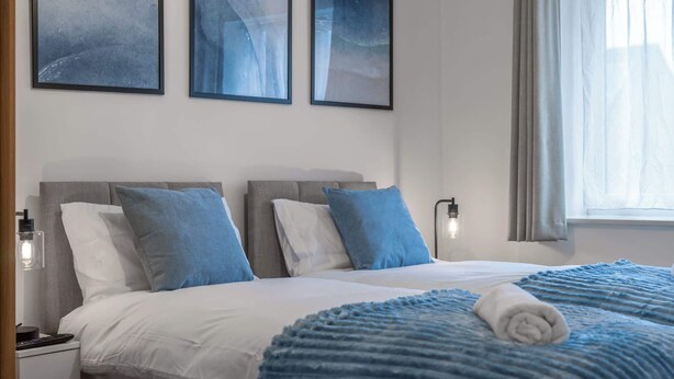 Ein Hotelzimmer mit Bett, Kissen, Decke, Nachttisch und Wandbildern.