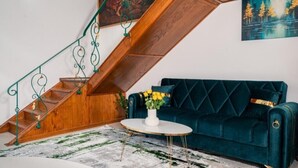 A staircase with green metal railings, a dark teal sofa, and a white vase with yellow flowers on a round table. - Apartament 1 (Timișoara)