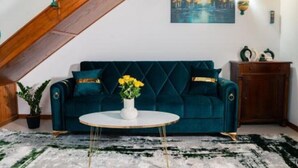 A room with a dark green sofa, a round white coffee table, and a painting of trees on the wall. - Apartament 1 (Timișoara)