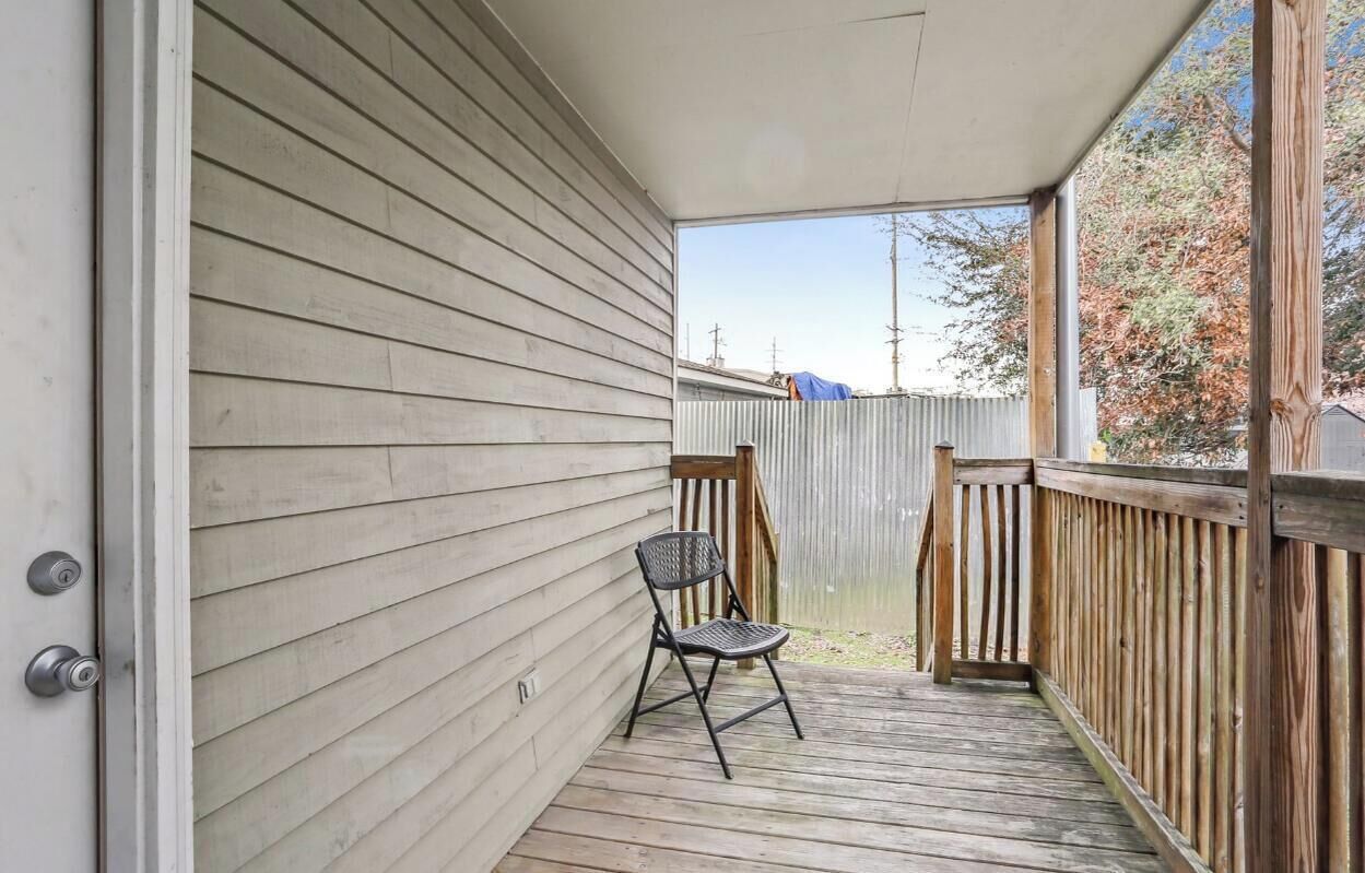 A covered porch with a wooden deck, a metal chair, and a view of a fenced yard.