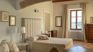 Un dormitorio con cama, mesitas de noche, cómoda, ventana con cortinas y cuadro colgado en la pared.